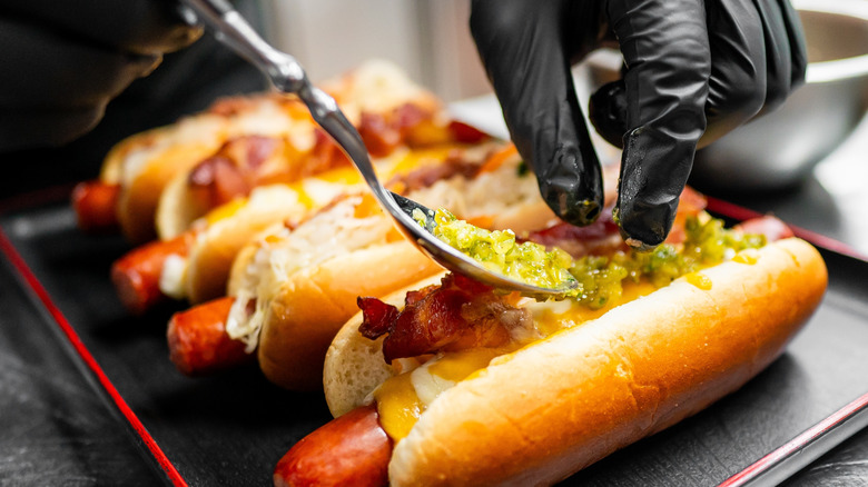 A chef spoons toppings onto a hot dog