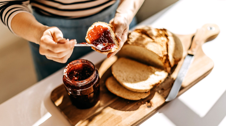 Hands smear jam onto a piece of bread