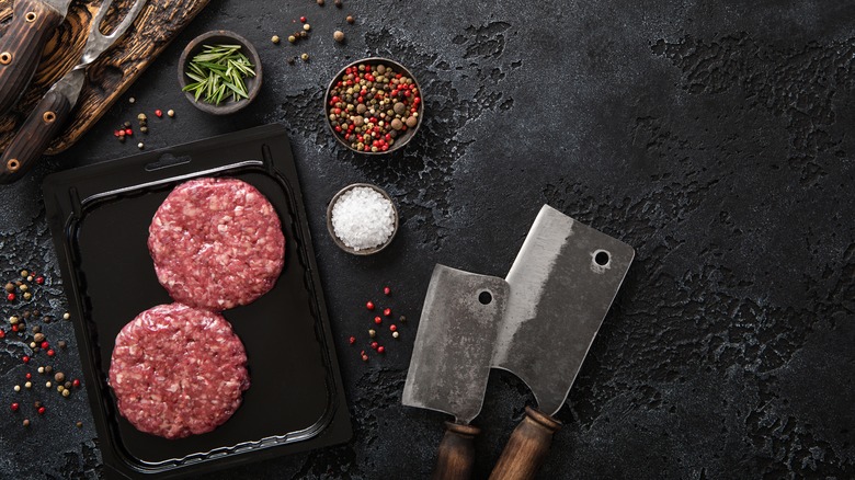 hamburger patties in a container next to meat cleavers