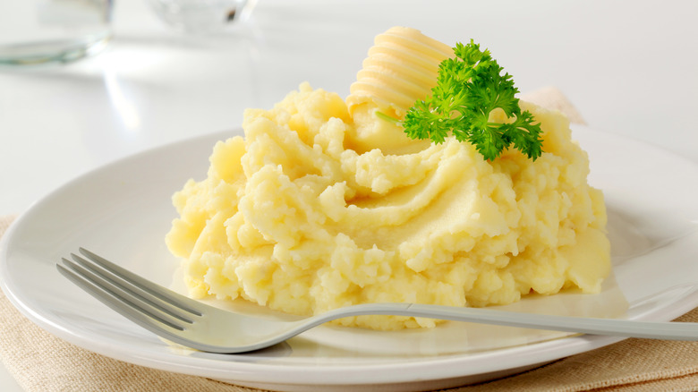 Mashed potatoes topped with butter and garnish on a plate with a fork