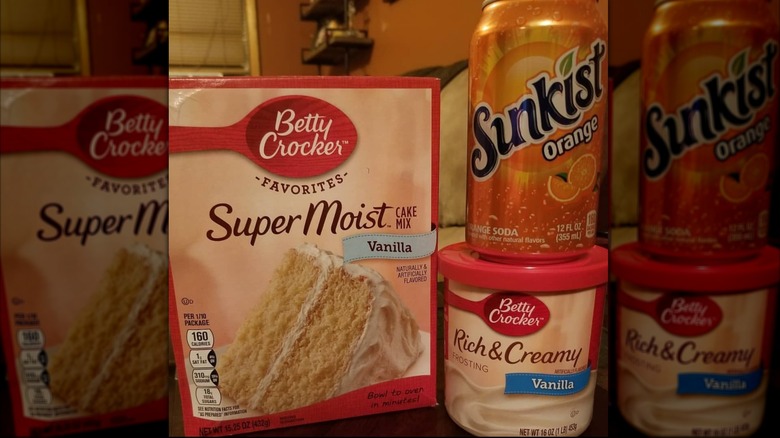 A box of vanilla cake mix with a can of Sunkist orange soda and frosting