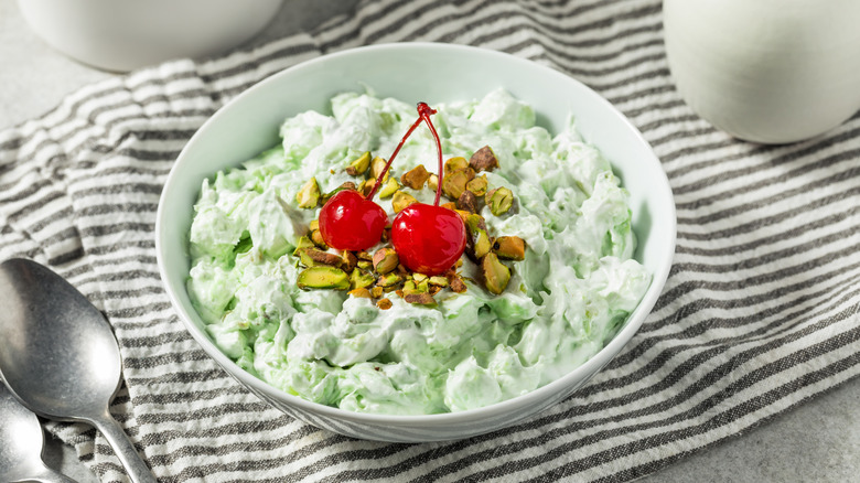 Watergate salad in a bowl topped with pistachios and maraschino cherries