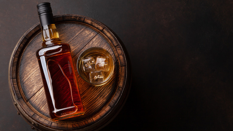 bottle and glass of bourbon on wooden barrel 