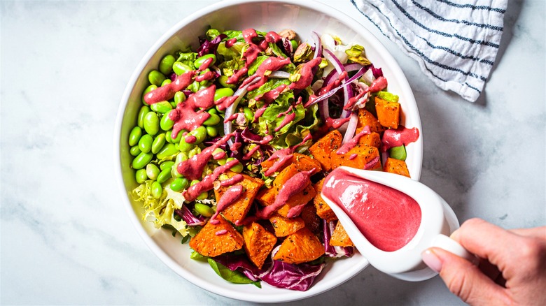 Hand pouring pink dressing on salad 