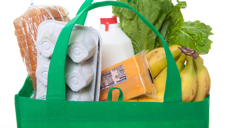 Eggs, bananas, cheese, lettuce, milk, and bread are in a green tote bag.