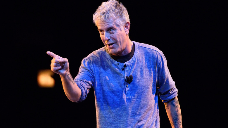 Anthony Bourdain pointing his finger while talking to someone in a dark room