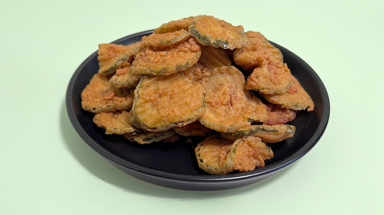 Texas Roadhouse Fried Pickles piled on a black plate against a green background