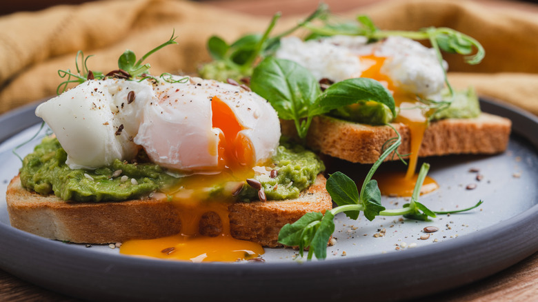 runny eggs benedict with avocado on rustic plate