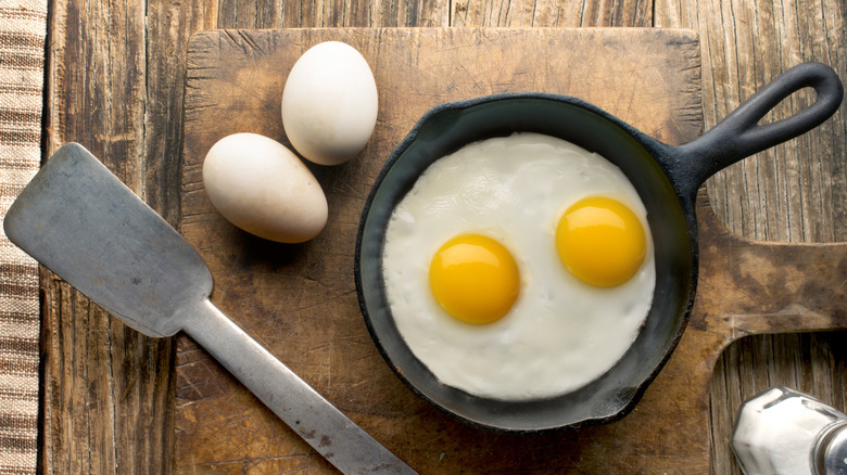 overhead shot of sunny-side up eggs in cast iron pan with whole eggs