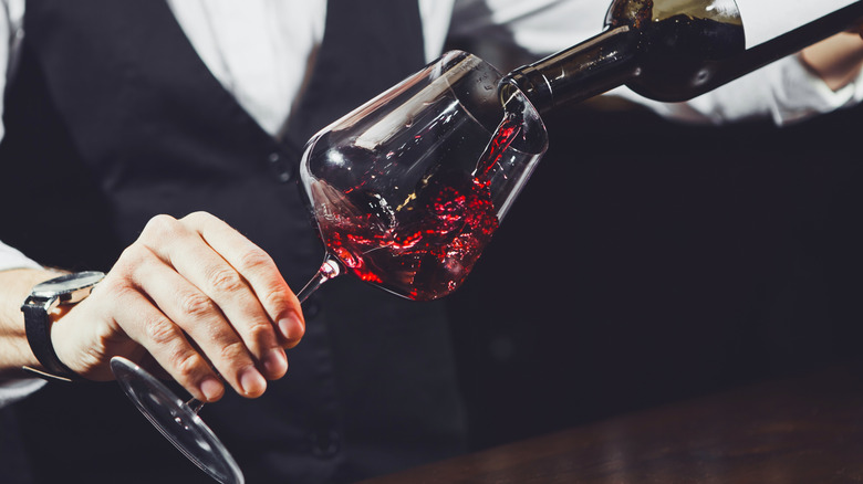 Person pouring red wine into a wine glass at an angle