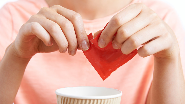 Hands adding artificial sweetener to coffee