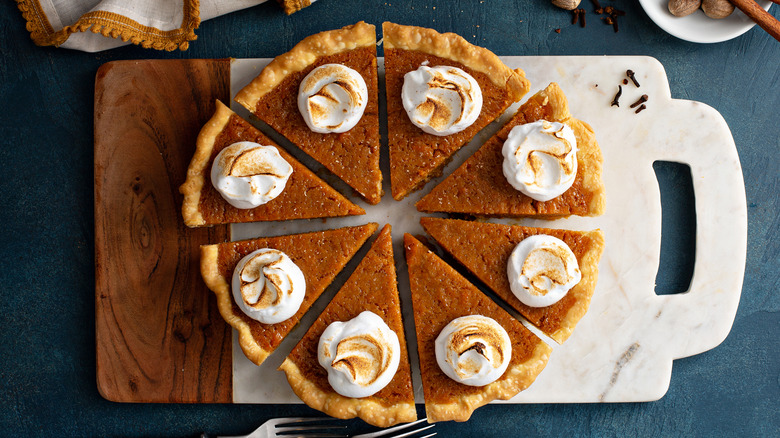 Whole, cut sweet potato pie with dollop of marshmallow fluff on a cutting board