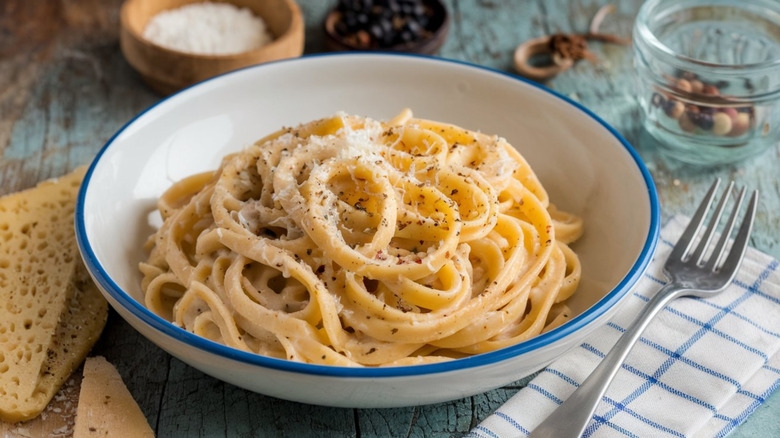 Cacio e pepe pasta in a white bowl surrounded by ingredients