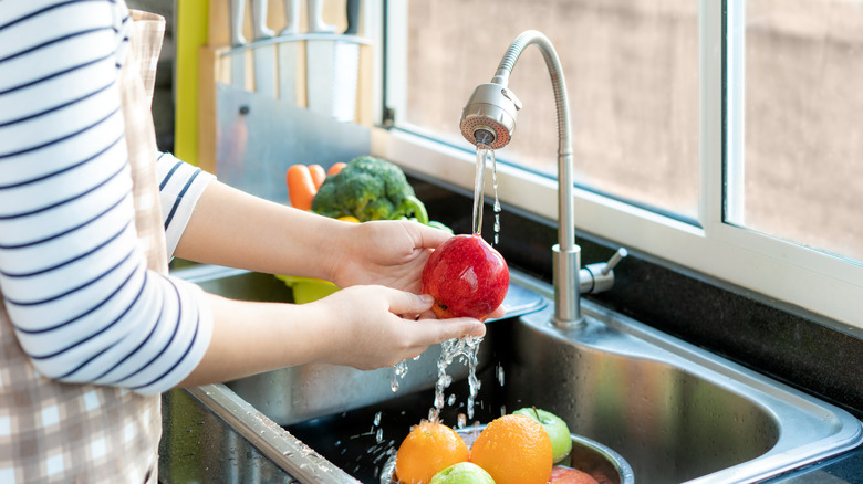 Woman holds apple under running water in sink