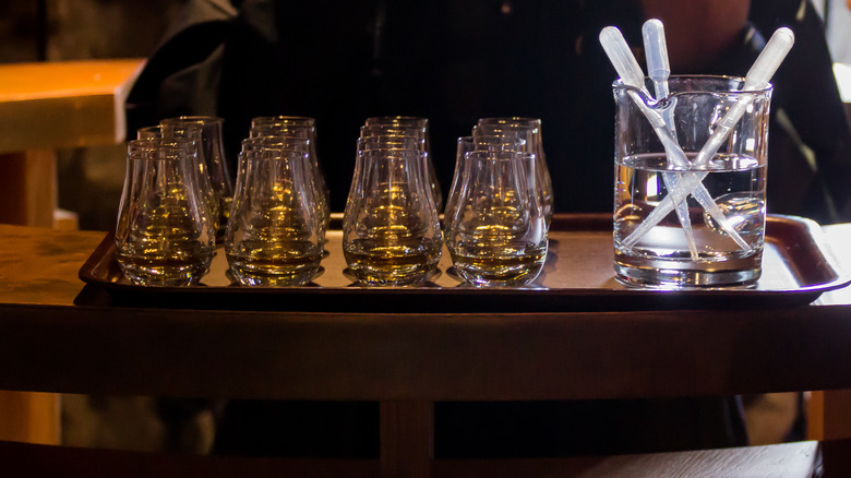 Set-up for a whiskey tasting session, with rows of whiskey in tulip glasses and pipettes of water