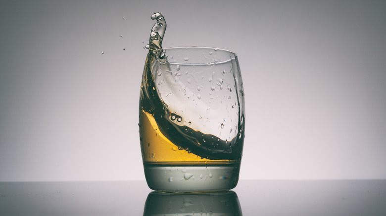 Glass of whiskey, with the whiskey swirling inside, some of it spilling from the top of the glass