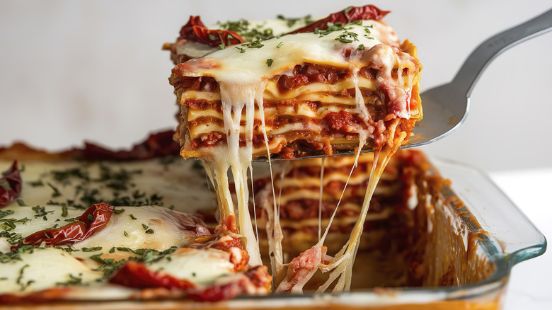 A slice of lasagna being lifted from the pan with a metal spatula, revealing layers of pasta and meat sauce