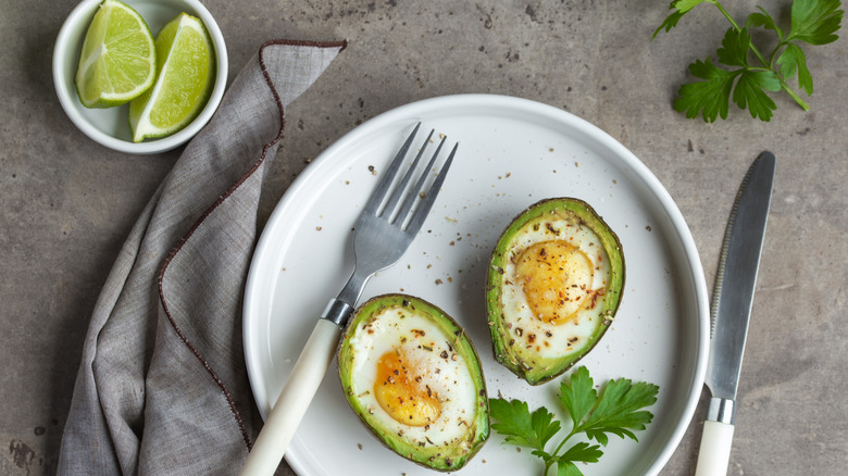 Baked egg in avocados with silverware and a side of lime