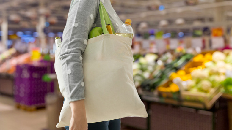 A person carrying a canvas bag full of groceries with a blurred background in a supermarket