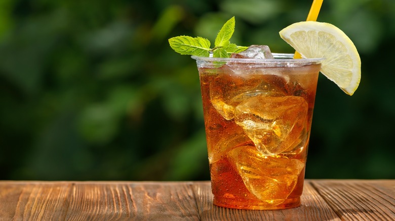 Plastic cup of iced tea with mint sprig, lemon slice, and straw