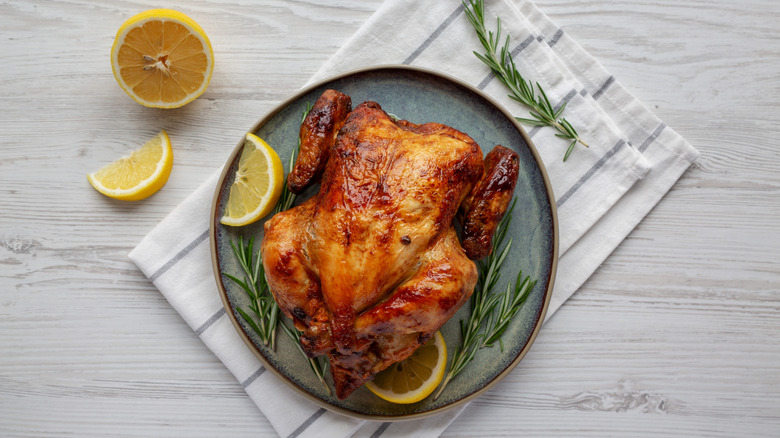 A rotisserie chicken with lemon wedges and rosemary sprigs