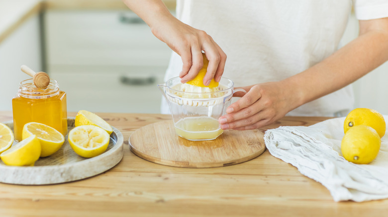 A person juicing lemons on a wooden table with a container of honey next to a bunch of halved lemons