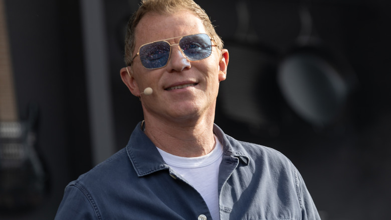 Bobby Flay smiling while wearing blue sunglasses and a face microphone