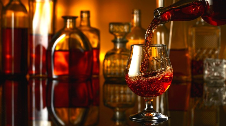 Brandy bottle pouring into glass with unfocused brand decanters in the background.