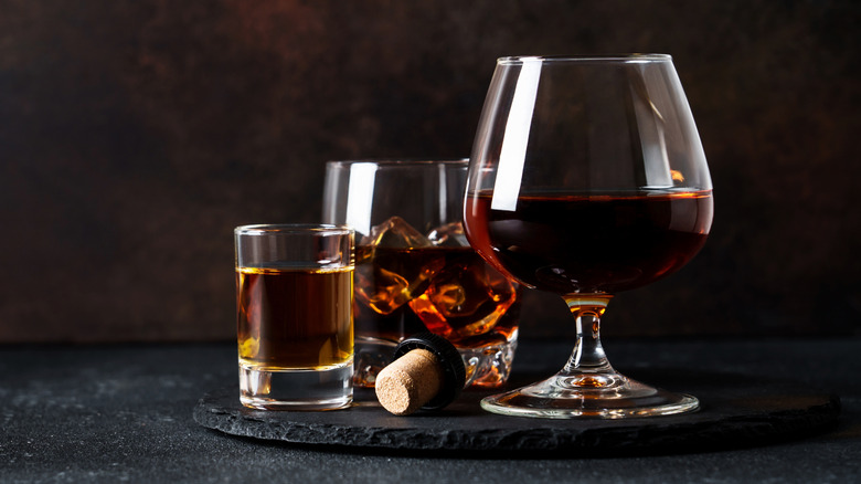 Glasses of brandy and bourbon on ice set against a dark background