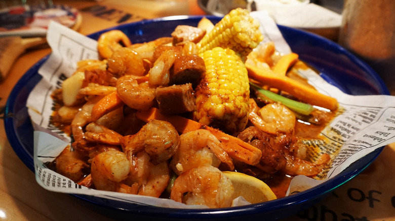 Steamed shrimp covered in a brown sauce with vegetables, sausage, french fries, and corn on the cob