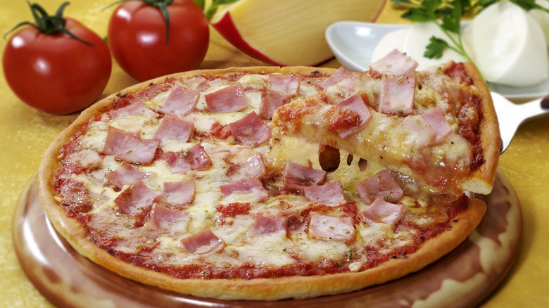 Cooked frozen pizza with ham and cheese and a slice being pulled out by a spatula