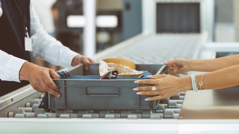 Person hands over personal items on plastic tray at TSA airport screening