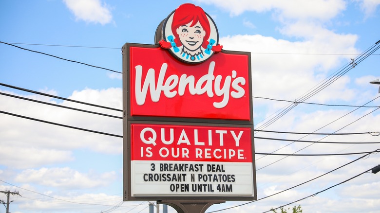 Wendy's sign during the daytime against a blue sky with white clouds and power lines in between