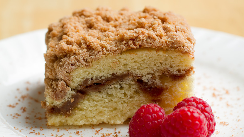Slice of coffee cake next to three raspberries