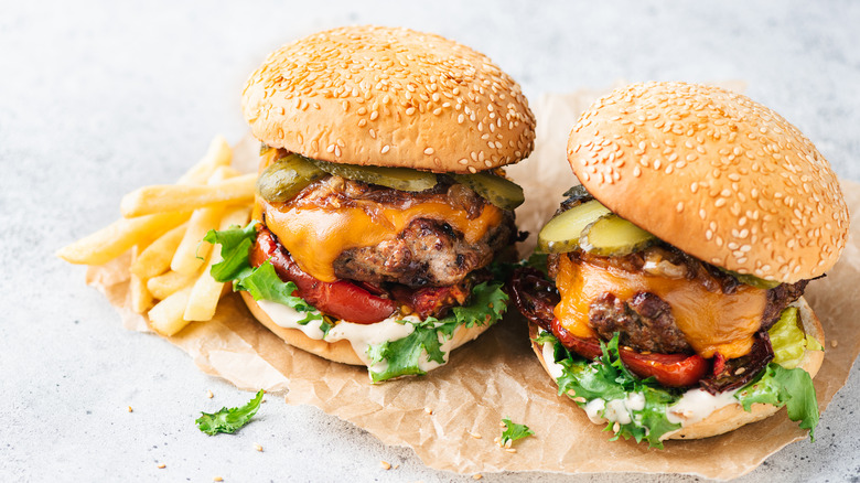 two hamburgers with pickles, cheese, and other condiments