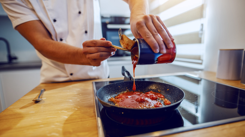 adding canned tomatoes to pan