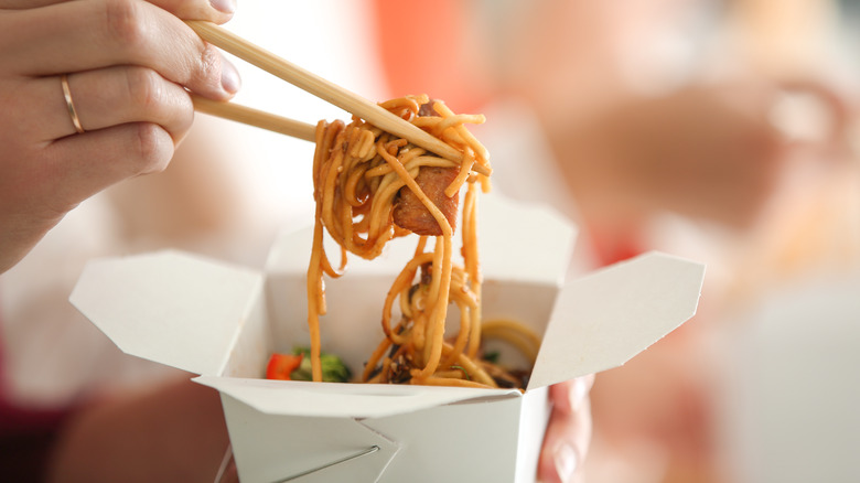 chopsticks lifting noodles from takeout box