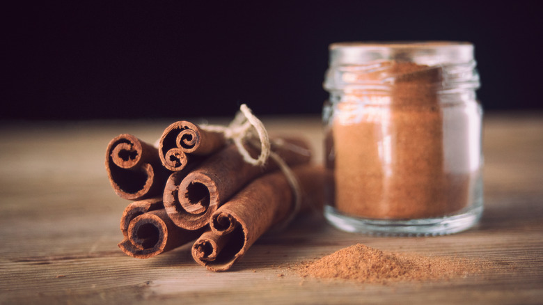 A bundle of cinnamon sticks and a jar of cinnamon powder on a wooden table