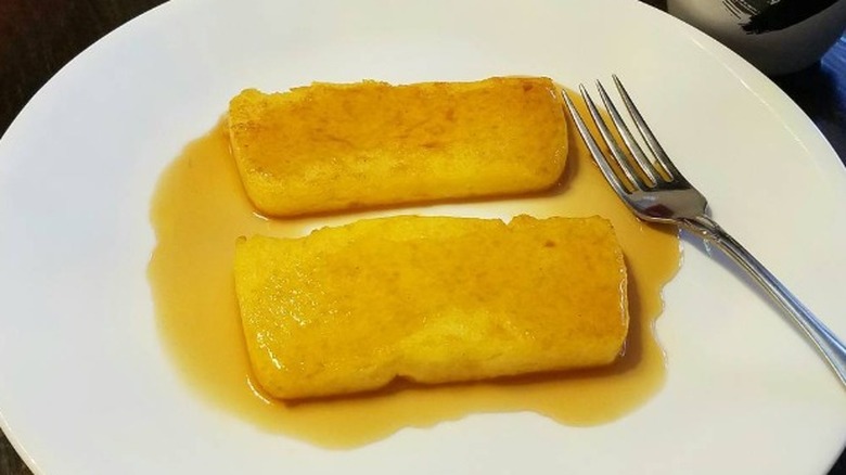 Fried cornmeal mush topped with maple syrup on a white plate with a fork