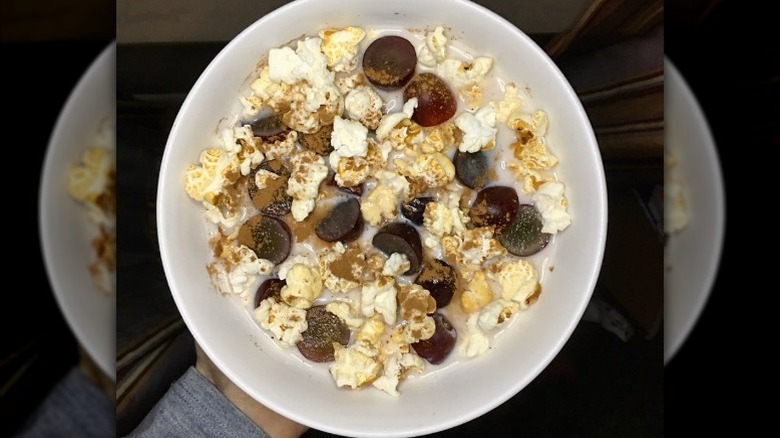A person holding a bowl of popcorn cereal with sliced grapes