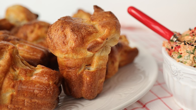 Popovers on a plate placed on a table with a spread in a bowl on the side