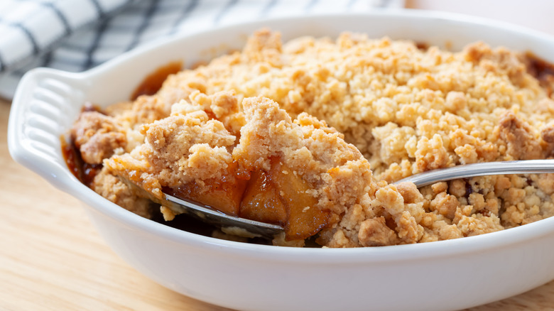 Spoon lifts a serving of apple crumble out of a baking dish
