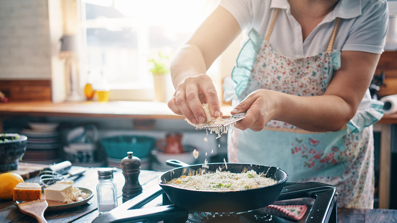 Woman grating cheese over pan