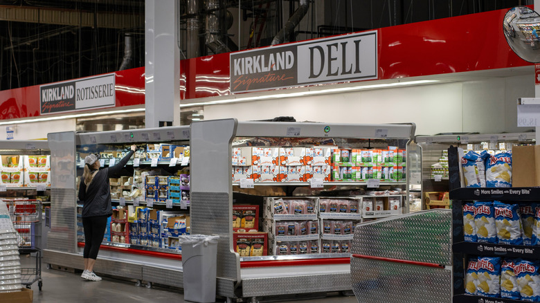 A person shopping in Costco with Kirkland Signature signs displayed above