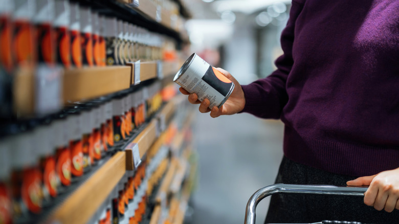 A person picks up a canned product and reads it in the grocery store