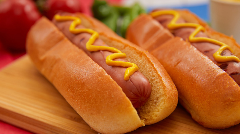 Two hot dogs with mustard next to each other on a cutting board