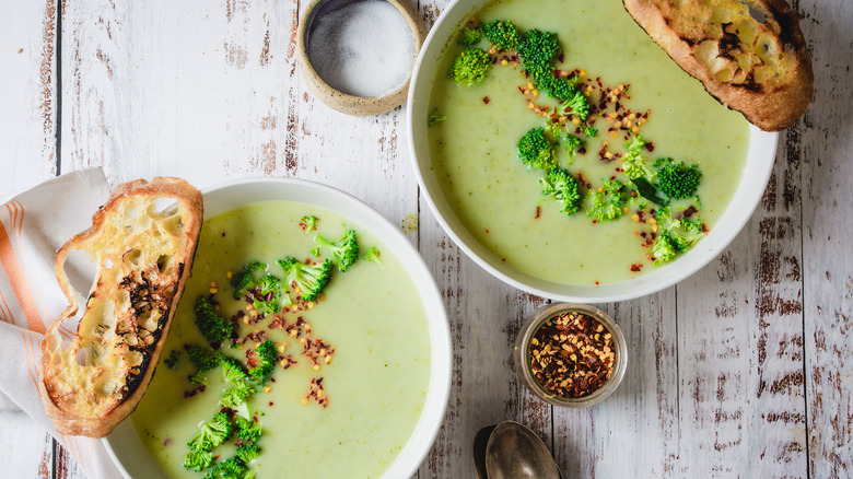 two plates of broccoli soup with bread and chili flakes