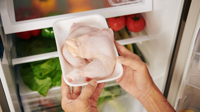 A pack of chicken quarters being removed from a refrigerator