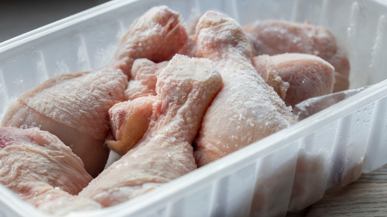Frozen chicken drumsticks defrosting in a plastic tray