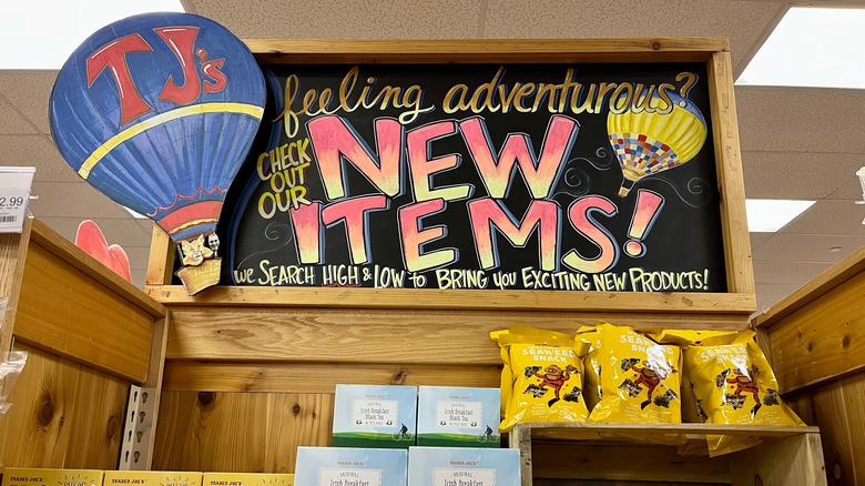 a chalkboard display at Trader Joe's with a hot air balloon labeled TJ's and the board reading feeling adventurous? check out our new items we search high and low to bring you exciting new products